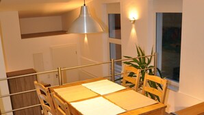 Un coin repas avec une table et des chaises en bois, un luminaire suspendu et une vue sur l’extérieur par une fenêtre.