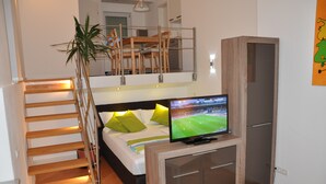 Une chambre à coucher avec un lit, un téléviseur posé sur un meuble en bois, un escalier et une plante.