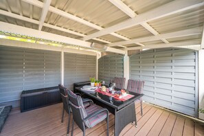 A covered patio area with a table set for dining, surrounded by wicker chairs.
