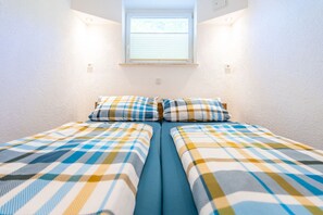 A twin room with two beds, a window with blinds, and a white textured wall.