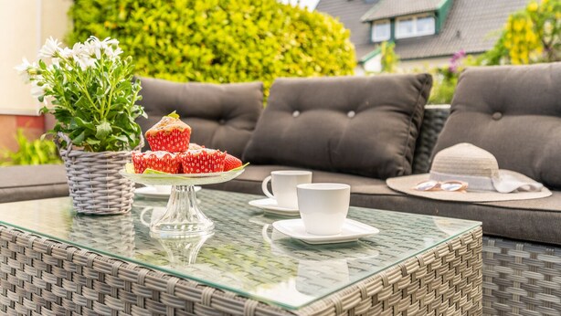 A glass-top table with a wicker basket, a white cup, a saucer, and a hat.
