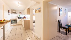 A compact kitchen with a microwave, oven, and sink, leading to a dining area with a table and chairs.