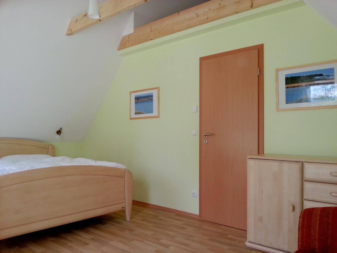 A bedroom with a bed, a wardrobe, and two framed pictures on the wall.