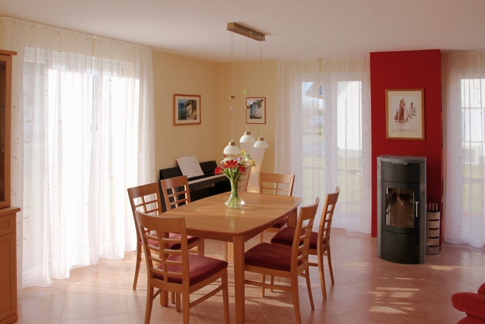 A dining area with a wooden table, chairs, a vase with flowers, a piano, and a fireplace.