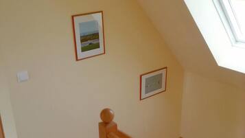Een trap die leidt naar een zolder met dakraam, houten leuning en twee ingelijste foto's aan de muur.