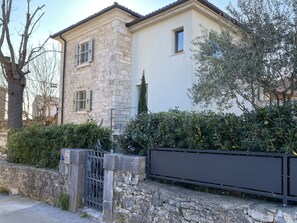 A stone building with a modern extension, a gated entrance, and surrounding greenery.
