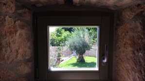 Una habitación con pared de piedra y ventana que da a un jardín con un árbol y otra pared de piedra.