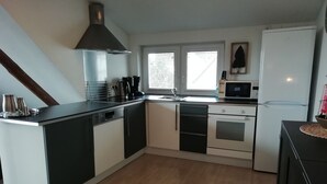 A modern kitchen with a central island, built-in oven, microwave, and a large window providing natural light. - Nice apartment with beautiful lake view and large garden (Waldeck)