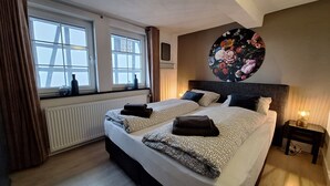 A bedroom with two beds, a radiator, a window with curtains, a wall-mounted picture, and a bedside table with a lamp. - Nice apartment with beautiful lake view and large garden (Waldeck)