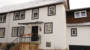 A two-story building with a stone foundation, a wooden door, and a black metal staircase leading to a porch with a roof. - Nice apartment with beautiful lake view and large garden (Waldeck)
