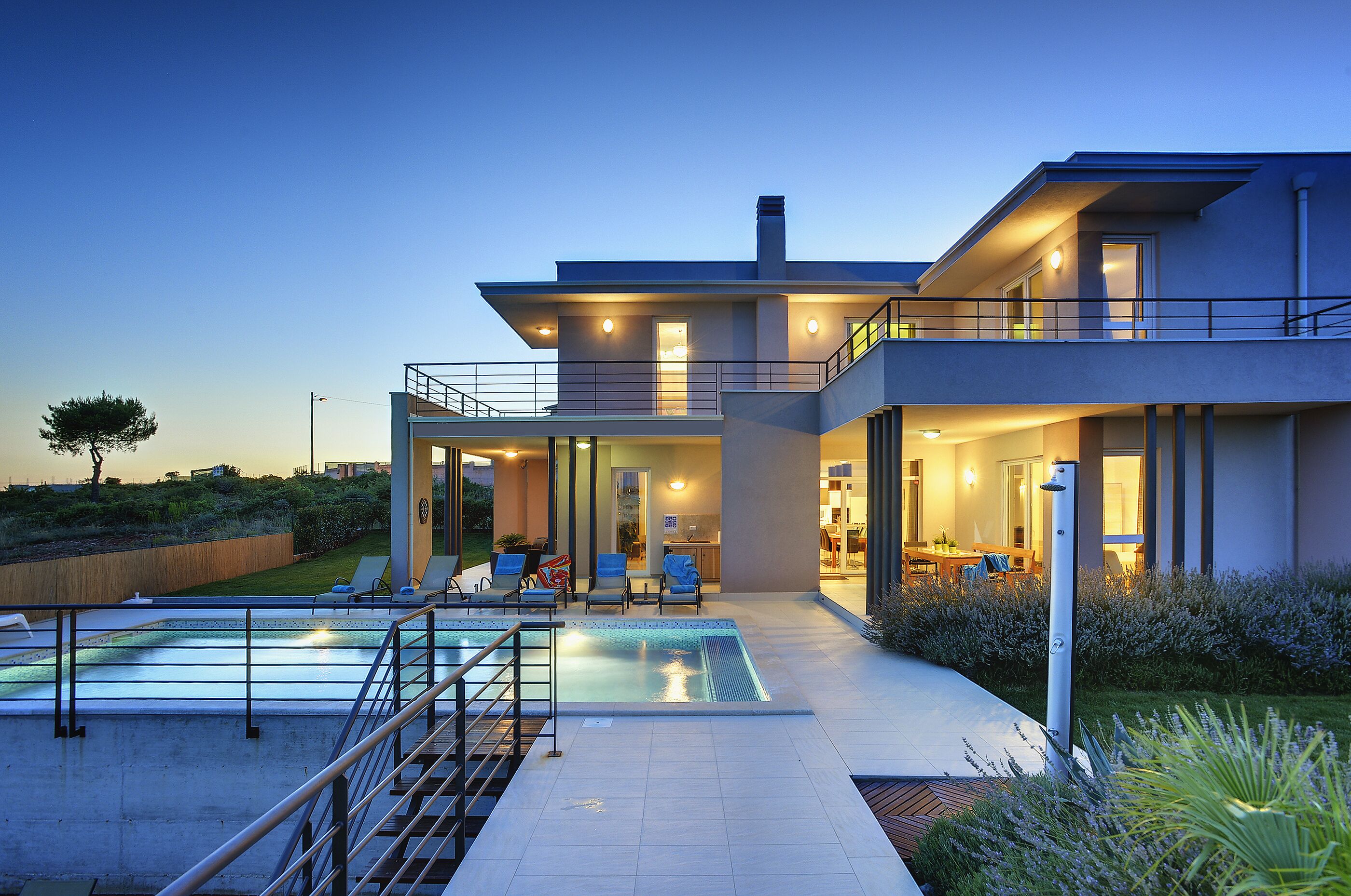 A modern two-story house with a swimming pool, outdoor seating, and a well-lit patio area.