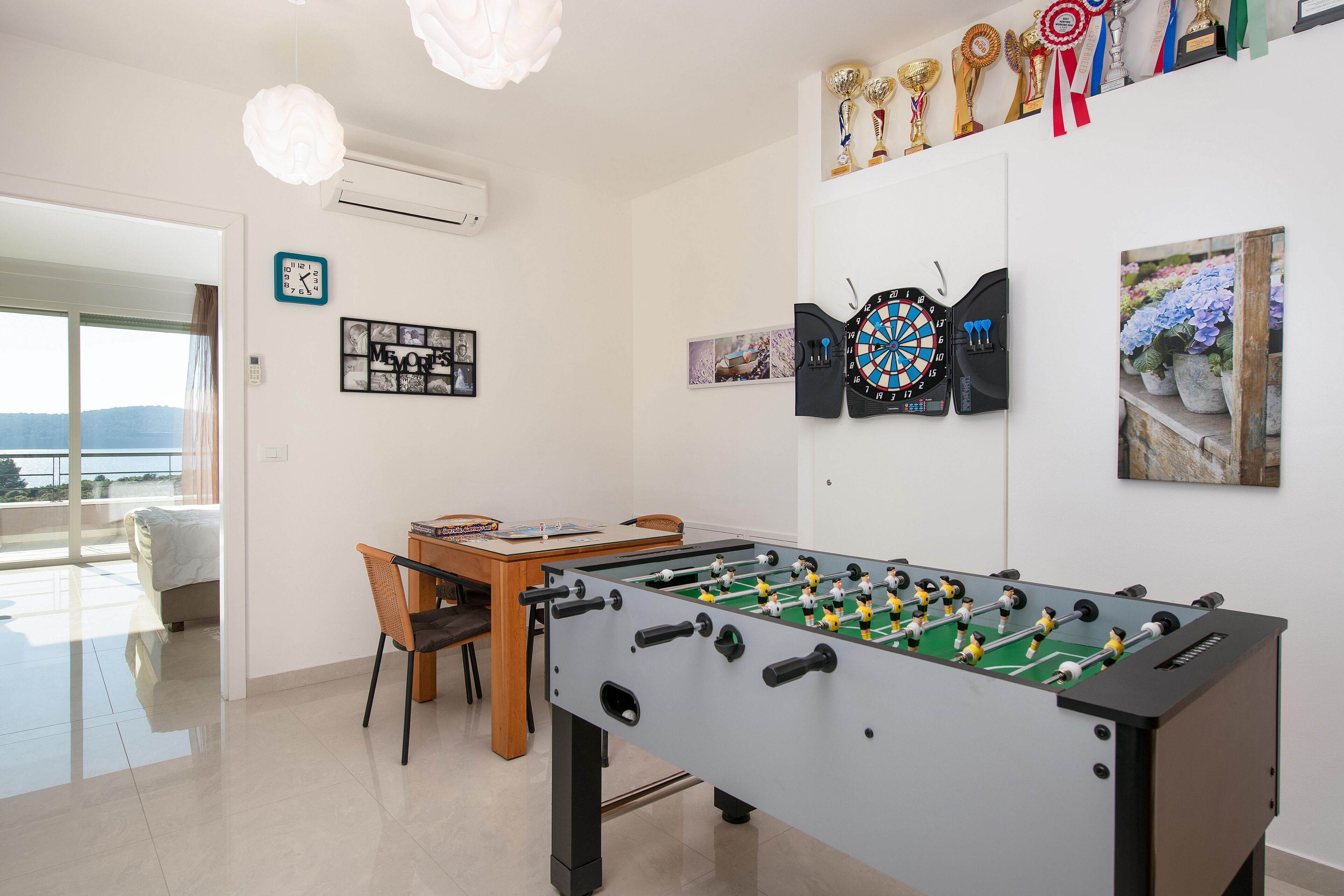 Una habitación con mesa de futbolín, dardos y un expositor de trofeos.