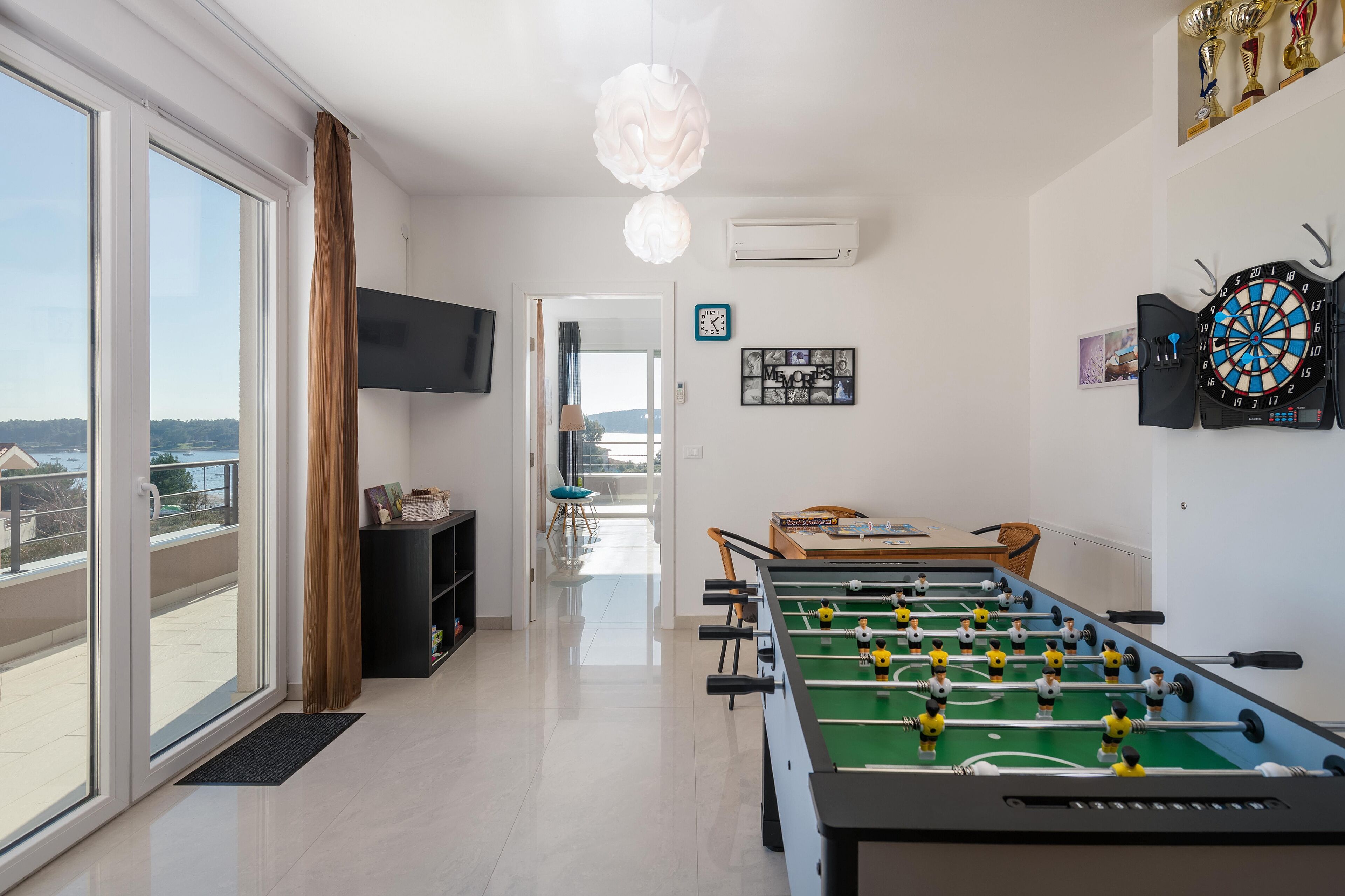 A modern living room with a foosball table, a flat-screen TV, and a dartboard.