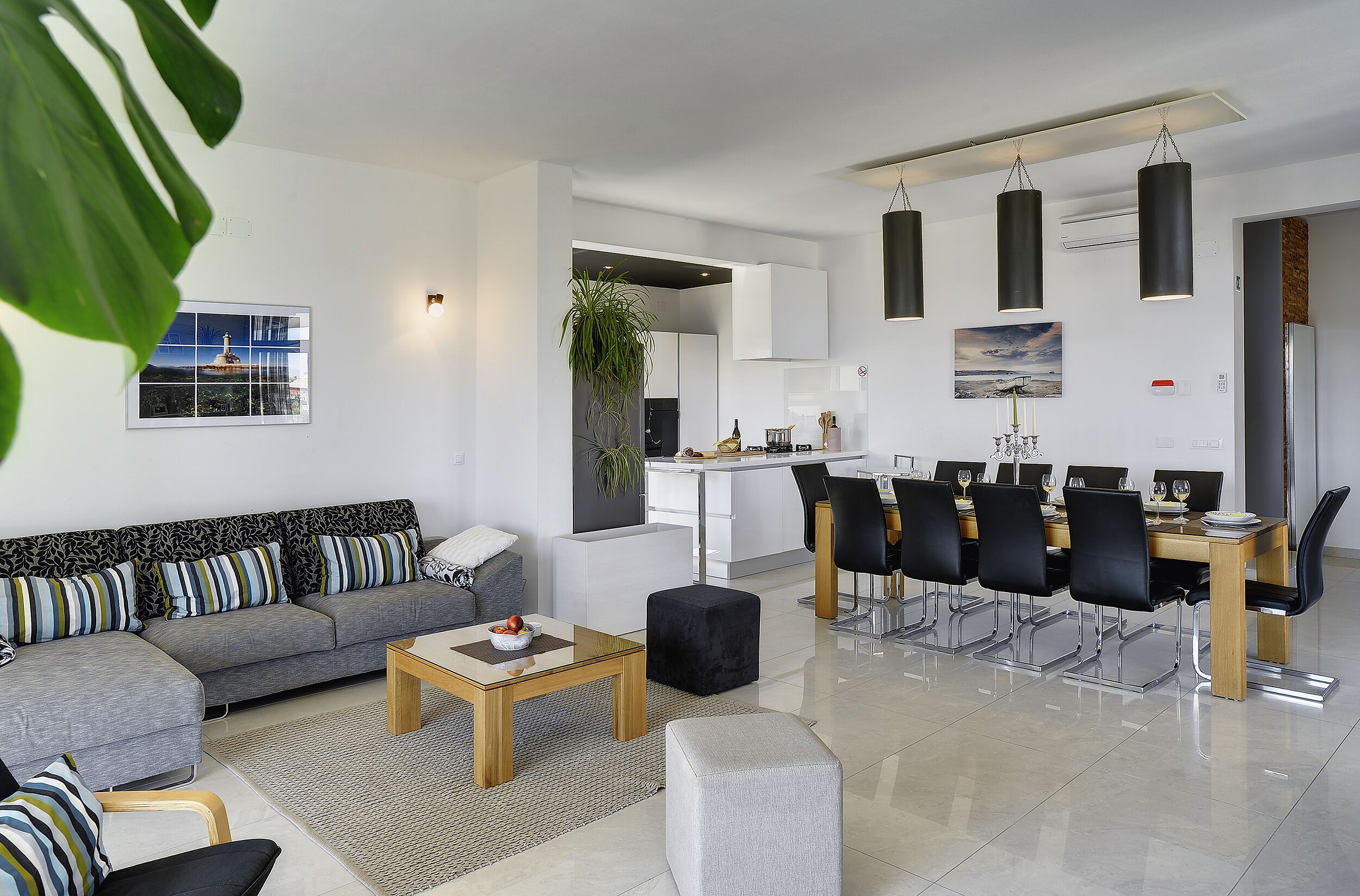 Een moderne woonkamer met een grijze bank, een houten salontafel, en een eethoek met een lange tafel en stoelen.