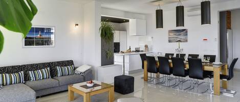 Ein modernes Wohnzimmer mit einem grauen Sofa, einem Holztisch und einem Essbereich mit einem langen Tisch und Stühlen.