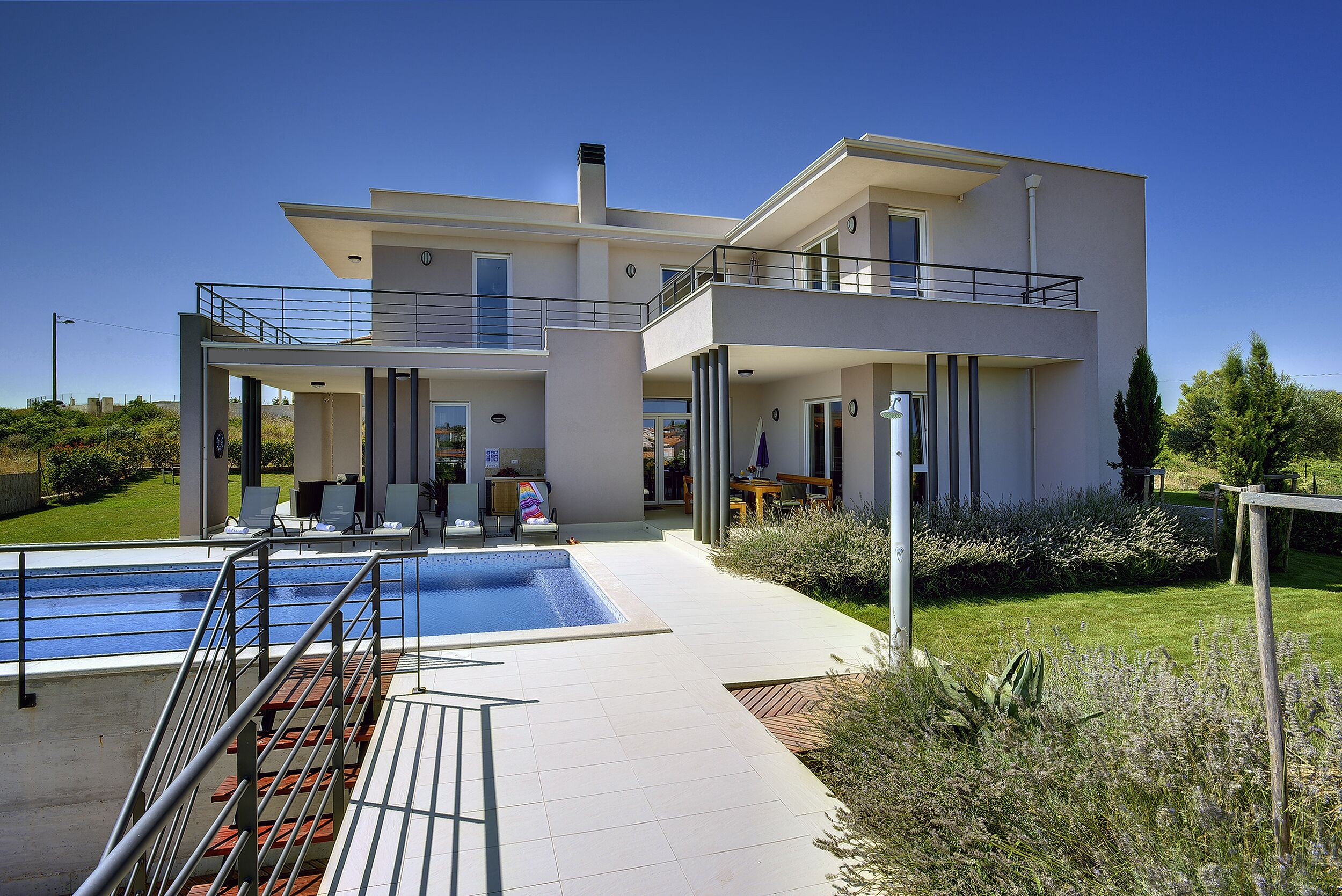 A modern two-story house with a swimming pool, outdoor seating, and a well-maintained garden.