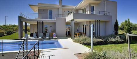 A modern two-story house with a swimming pool, outdoor seating, and a well-maintained garden.