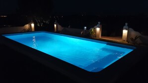 Une piscine rectangulaire dont l’intérieur est illuminé en bleu, entourée de petits murets et de quelques plantes.