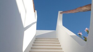 Un escalier montant, avec des murs blancs et un ciel bleu clair au-dessus.