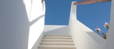 A staircase leading upwards with white walls and a clear blue sky above.