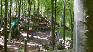 Un área boscosa con un puente colgante, construcciones de madera y un sendero de tierra.
