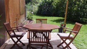 Eine Terrasse mit Holztisch und vier Stühlen, umgeben von einem Garten mit Holzlattenzaun und Pflanzen.