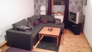 Ein Wohnzimmer mit einem dunkelgrauen Sofa, einem Holztisch und einem Fernseher auf einem Schrank.