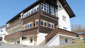 Ein zweistöckiges Gebäude mit einem Balkon im oberen Geschoss und einer Treppe, die zum Eingang führt.