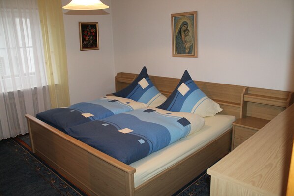 A neatly made bed with blue and white bedding, a wooden headboard, a bedside table, and a wall-mounted picture. - 120m² apartment with level in Kirchberg, in the heart of the Bavarian Forest. (Kirchberg im Wald)