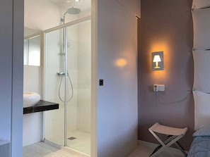 Un baño moderno con ducha envuelta en cristal, un lavamanos blanco y un perchero para toallas.
