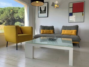 A modern living room with a glass coffee table, a mustard-colored armchair, a gray sofa with yellow cushions, a framed picture on the wall, and a geometric abstract painting. - Villa Sonni - Three Bedroom Villa, Sleeps 6 (L'Escala)
