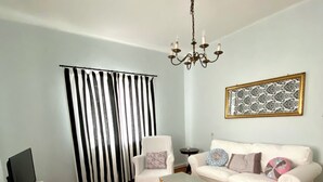 A living room with a white sofa, a small side table, a TV, a chandelier, a patterned rug, and a black and white striped curtain. - Lovingly furnished holiday home in the small wine-growing village (Landau in der Pfalz)