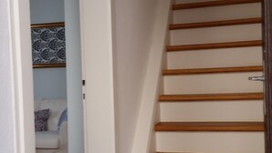 A staircase with wooden steps and white walls, leading to a room with a patterned wallpaper and a white sofa. - Lovingly furnished holiday home in the small wine-growing village (Landau in der Pfalz)