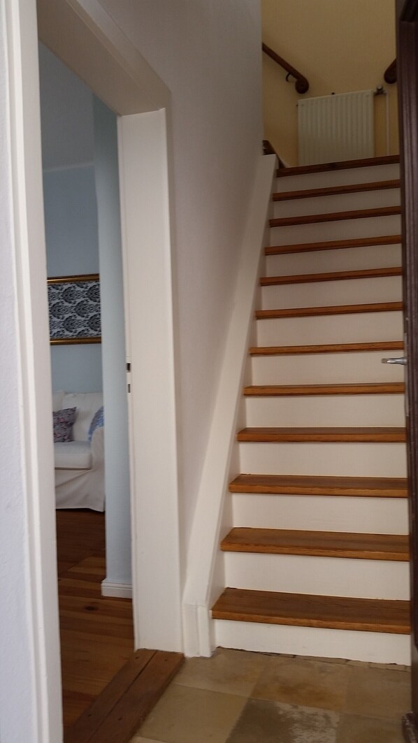 Una escalera con escalones de madera y paredes blancas que conduce a una habitación con papel tapiz estampado y un sofá blanco.