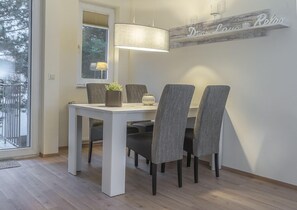 Uma área de refeições com mesa branca, cadeiras estofadas cinzentas, um candeeiro pendente e um letreiro decorativo na parede.