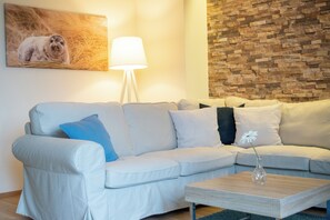 Uma sala de estar moderna com um sofá de cor clara, uma luminária e uma parede de pedra.