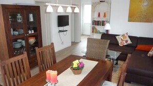 A dining area with a wooden table, two candles, and a flower centerpiece. There is a bookshelf with books and decorative items in the background. - family-friendly, comfortable accommodation, 2 terraces, 200 m to the beach (Neustadt in Holstein)