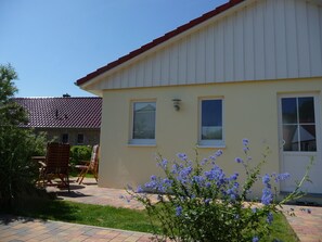 A two-story building with a red roof, a front porch with a wooden bench, and a small garden with blue flowers.