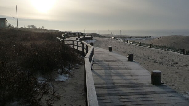A wooden boardwalk leading to a beach with a fence and a lamp post. - family-friendly, comfortable accommodation, 2 terraces, 200 m to the beach (Neustadt in Holstein)