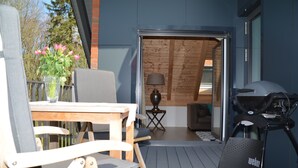 Um deck externo com mesa, cadeiras, churrasqueira e luminária.