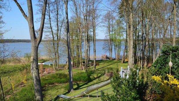 Um parque à beira de um lago, com gramado, árvores e um escorrega de metal.