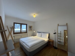 Ein Schlafzimmer mit Bett, Fenster, Heizkörper, Spiegel und Holzboden.
