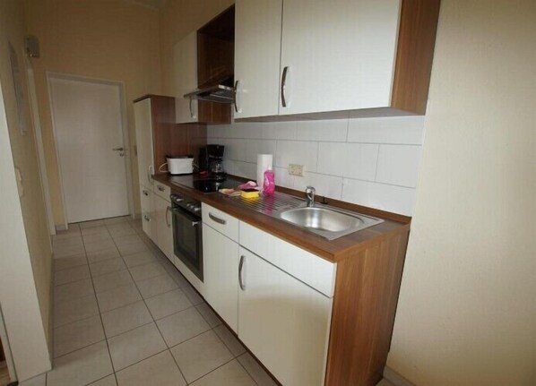 A compact kitchen with white cabinets, a wooden countertop, a stainless steel sink, and a coffee maker.