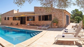 Villa de pedra amb piscina, zona de seients a l'aire lliure i terrassa coberta.