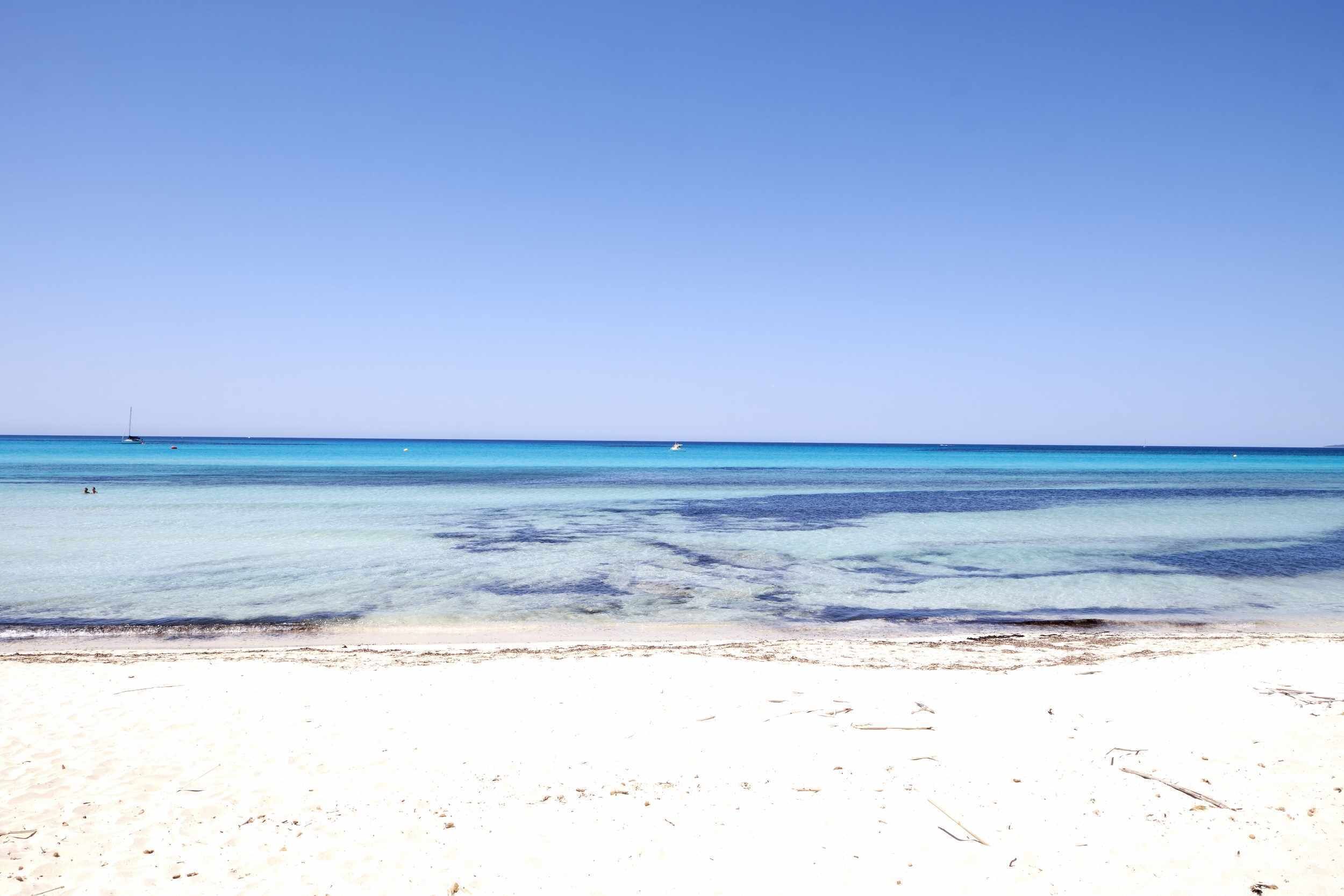 A beach with clear blue water and a sandy shore.