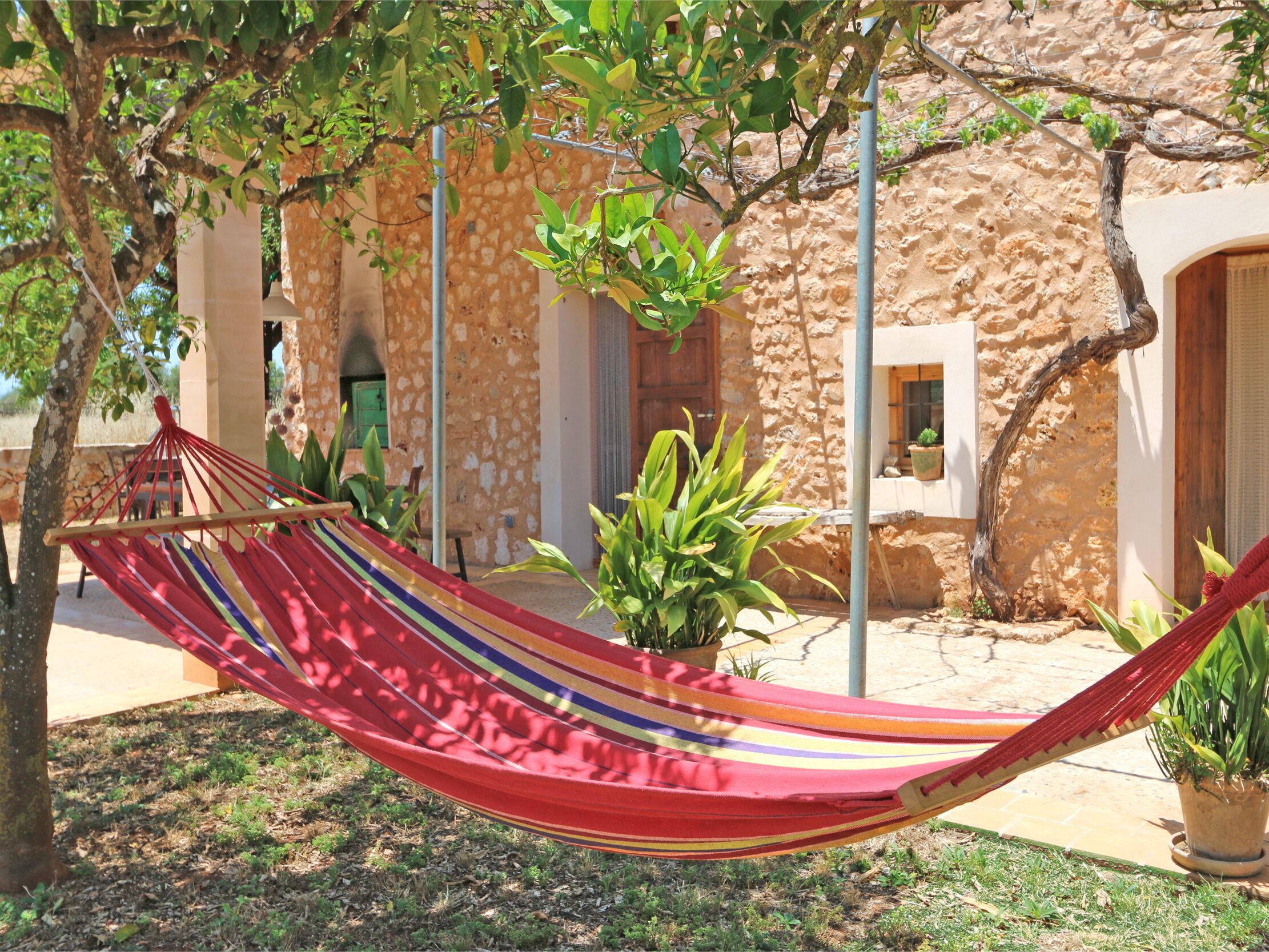 Una hamaca en un patio con paredes de piedra y plantas en macetas.