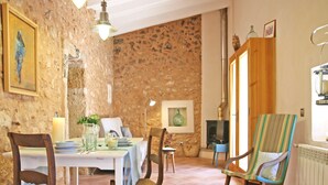 A rustic dining room with a stone wall, wooden furniture, and a traditional stove.
