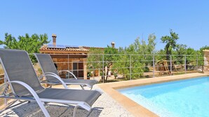 A poolside area with lounge chairs, a pool, and a building with a tiled roof.
