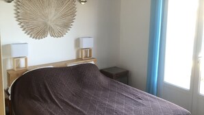 Une chambre avec un plafond en bois, un grand élément décoratif mural, un lit recouvert d’une couvre-lit à motifs, des tables de chevet avec des lampes et une fenêtre avec des rideaux.