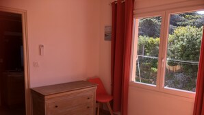 Une pièce avec une commode en bois, une chaise rouge, une fenêtre avec des rideaux rouges et une vue sur la verdure à l’extérieur.